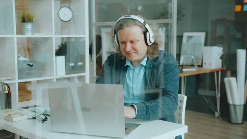 Un homme, casque sur les oreilles, travaille sur un ordinateur portable dans un bureau