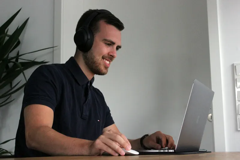 Une personne suit un cours en visioconférence depuis son bureau, casque sur les oreilles